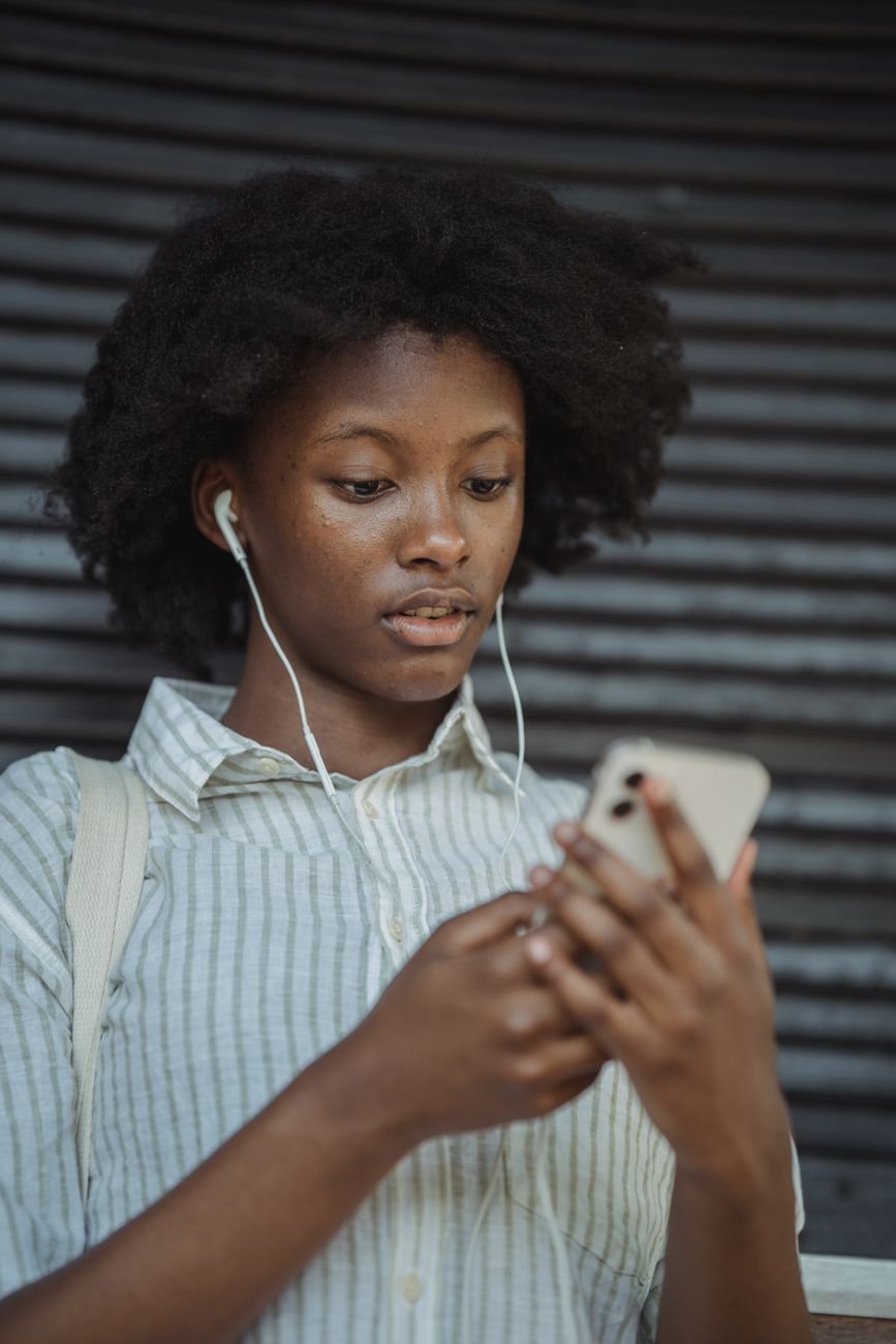 Young African woman using smartphone outdoors with earbuds